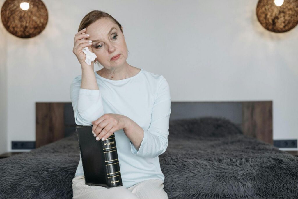 A woman sitting on a bed holding a photo album, looking emotional as she reflects on memories.